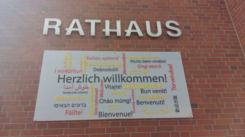 Willkommensschild in vielen unterschiedlichen Sprachen an der Außenwand des Rathauses