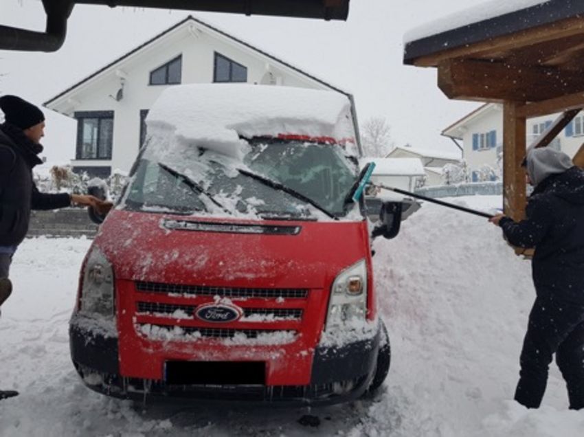 Zwei Personen befreien einen Kleinbus vom Schnee